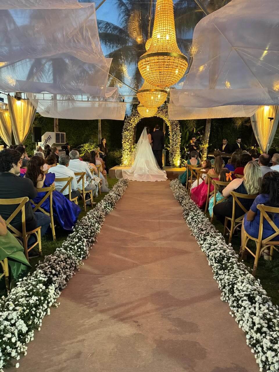 Altar de casamento noturno ao ar livre, iluminado por lustres de cristal pendentes em estrutura metálica e passarela decorada.
