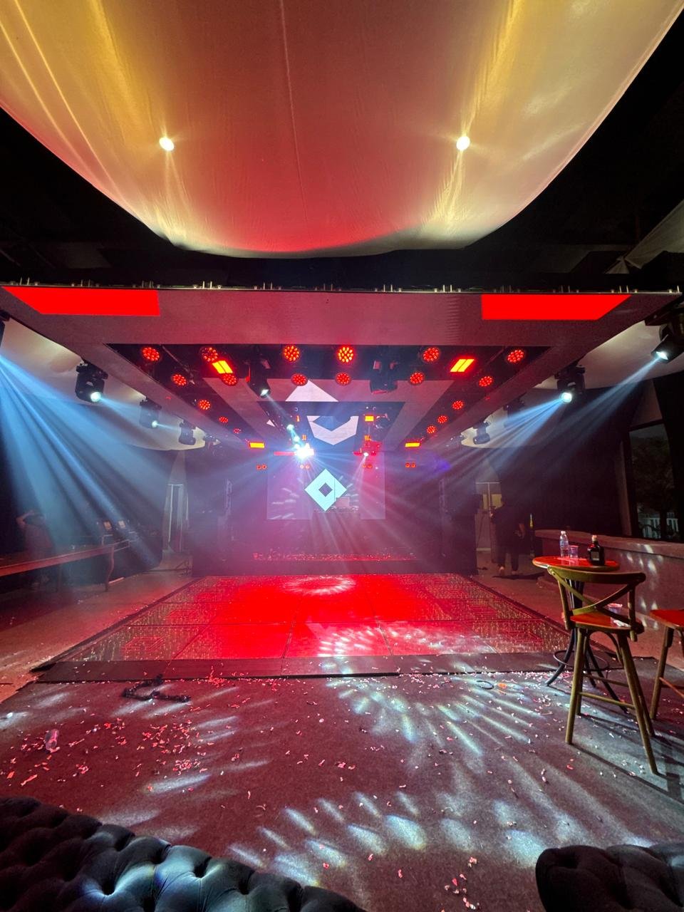 Pista de dança moderna com iluminação vermelha intensa, estrutura de grid no teto e moving heads projetando feixes de luz.